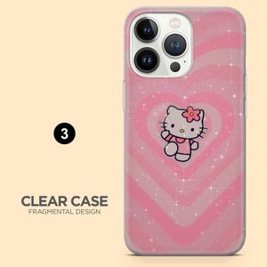 Op de afbeelding: Transparante telefoonhoes met een roze hartontwerp en een Hello Kitty-afbeelding. De hoes heeft een glittereffect en de tekst "CLEAR CASE FRAGMENTAL DESIGN". De telefoonhoes heeft een uitsparing voor een drievoudige cameralens.