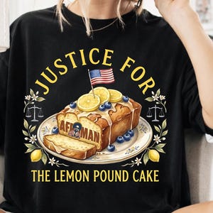 Puede incluir: Camiseta negra con un gráfico de bizcocho de limón adornado con arándanos, rodajas de limón y una pequeña bandera estadounidense. El texto dice "JUSTICE FOR THE LEMON POUND CAKE".
