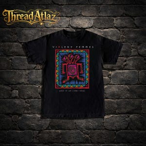 May include: Black t-shirt featuring a colorful graphic design with the text "VIOLENT + FEMMES" and "ADD IT UP (1981-1993)". The design includes a central figure with three heads and geometric patterns.