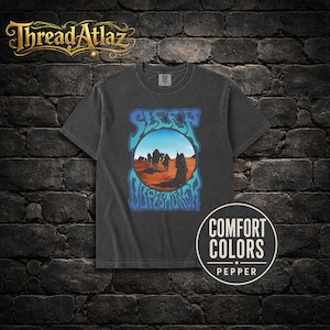 Peut inclure: Un t-shirt gris anthracite à manches courtes avec un motif circulaire représentant un paysage désertique, des silhouettes marchant sur du sable orange sous un ciel bleu. Le texte SLEEP et DROPESMOKER est écrit en bleu autour du cercle.
