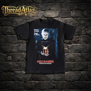 May include: Black t-shirt featuring a movie poster design for "Hellraiser." The design includes the film's title, a character image, and the tagline "He'll tear your soul apart." The shirt also has the text "Demon to some. Angel to others."