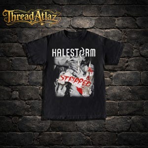 Op de afbeelding: Zwart t-shirt met de bandnaam "HALESTORM" in wit boven een grafische afbeelding en het woord "STRIPPED" in rood. Het shirt heeft een distressed look en het merk "ThreadAtlaz" staat in goudschrift bovenaan.