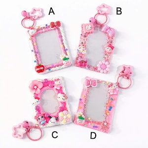 May include: Four pink and white decorative photo frame keyrings. Each frame has a rectangular shape with a clear centre and is adorned with various embellishments like bows, flowers, and cartoon characters. Each keyring has a pink ring and charm.