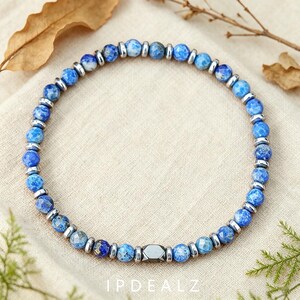Pode incluir: Uma pulseira de contas com contas redondas de pedra azul facetada alternadas com pequenos espaçadores cilíndricos de metal prateado. As contas exibem vários tons de azul com padrões manchados dispostos em formato circular.