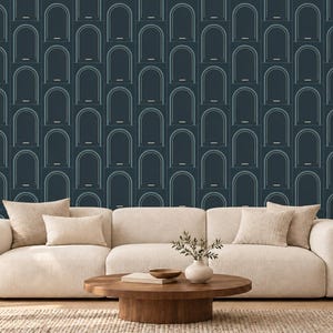 May include: A cream-colored sofa with four matching throw pillows sits in front of a dark blue wallpaper featuring a repeating pattern of thin, light blue arched doorways. A round wooden coffee table holds a small vase and a book.