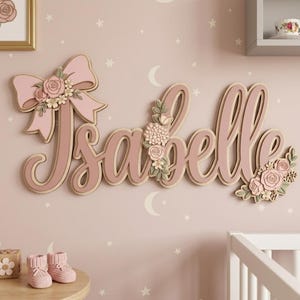 May include: A wall-mounted wooden sign featuring the name Isabelle in a cursive script, decorated with layered pink roses, green leaves, and a large pink bow. The letters are finished in shades of pink and beige, creating a dimensional effect.