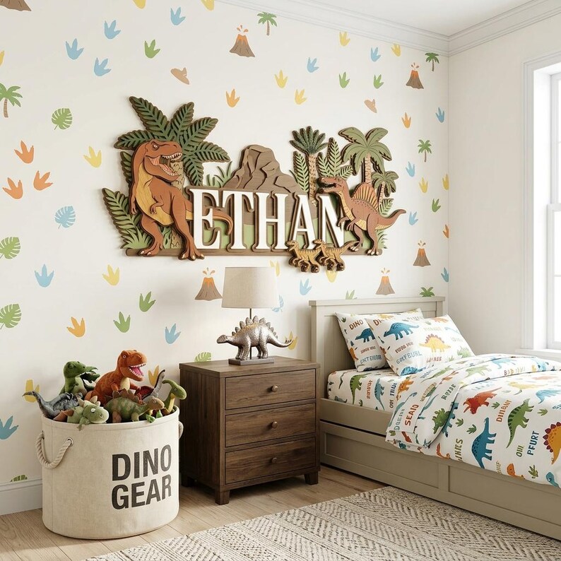 Puede incluir: Un dormitorio con tem&aacute;tica de dinosaurios con un letrero de madera con el nombre "ETHAN". La habitaci&oacute;n cuenta con una cama con ropa de cama con estampado de dinosaurios, una mesita de noche con una l&aacute;mpara de dinosaurio y un cubo de almacenamiento "DINO GEAR".