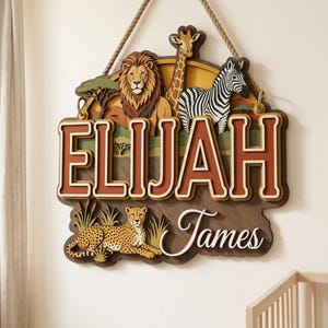 May include: A wooden sign featuring a lion, giraffe, and zebra, with the name "Elijah" in large, layered letters. A cheetah is at the bottom. The sign is designed with a safari theme and is suspended by a rope.