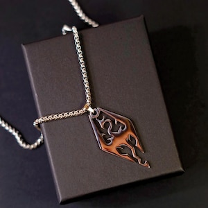 Può includere: Una collana con ciondolo in metallo color argento caratterizzata da un pendente a forma di diamante con un intricato design a drago traforato. Il ciondolo è appeso a una catena a maglia quadrata abbinata, con una finitura metallica lucida.