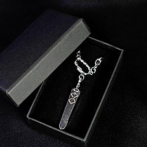 May include: A silver-colored pendant necklace with a rectangular bar pendant featuring geometric designs, presented in an open black box. The necklace has a chain with a twisted design near the clasp.