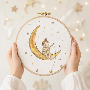 Patrón de punto de cruz de un adorable bebé en la luna, PDF para habitación infantil celestial, arte caprichoso de pesca de estrellas.