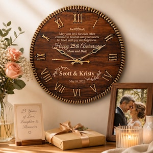 Peut inclure: Une horloge murale ronde en bois au grain brun foncé, dotée de chiffres romains dorés, d'aiguilles dorées et d'une bordure tressée dorée. Elle est gravée avec "Happy 25th Anniversary", "Mom and Dad", "Scott & Kristy" et "May 16, 2022".