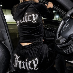 May include: A black velour tracksuit consisting of a long-sleeved hooded jacket and matching trousers. Both pieces feature the word Juicy written in silver-toned rhinestones across the back, with the jacket text on the upper back and the trousers text on the seat.