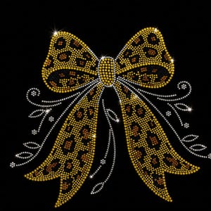Op de afbeelding: Een decoratief strikontwerp bestaande uit glinsterende strass-steentjes tegen een zwarte achtergrond. De strik heeft een goud en bruin luipaardpatroon, geaccentueerd door delicate, wervelende zilveren strass-ranken en kleine bloemdetails.