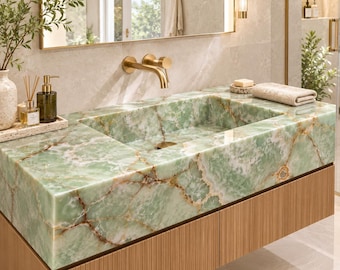May include: A rectangular bathroom sink made of light green onyx stone with prominent white and brown veining. The sink features a wall-mounted brushed gold faucet and is integrated into a vanity cabinet with a light wood, vertically ribbed front.