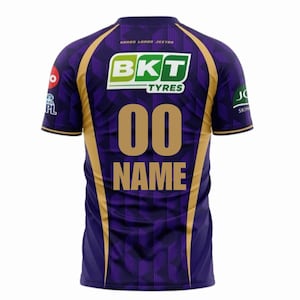 Puede incluir: Camiseta deportiva morada y dorada con el número "00" y la palabra "NAME" en dorado. La camiseta tiene un patrón geométrico y presenta el logotipo "BKT TYRES" y otros logotipos de patrocinadores. La camiseta es de manga corta.