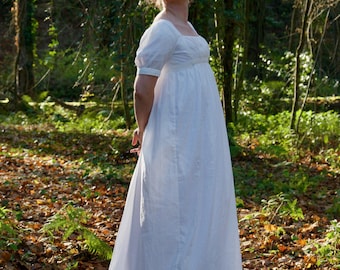 May include: A floor-length white dress featuring short puff sleeves, a square neckline, and a high empire waistline. The garment is crafted from a lightweight fabric with a subtle vertical pinstripe pattern, falling into a full, flowing skirt.