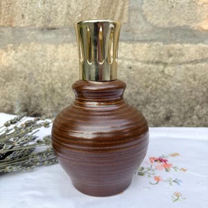 May include: A brown ceramic fragrance lamp with a rounded, ribbed body and a shiny gold-toned metal crown top. The lamp features a smooth, glossy finish and a wide base that tapers towards the neck, topped with a decorative vented metal cap.