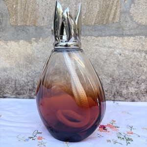 May include: A teardrop-shaped glass fragrance lamp with a gradient color transition from clear at the top to a deep amber-brown at the base. It features a silver-toned metal crown-shaped burner cap and a thick white cotton wick inside.