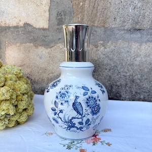 May include: A white ceramic fragrance lamp with a rounded body featuring a blue floral and bird pattern. The lamp has a silver-coloured metal crown top with vertical cutouts. The design includes detailed blue illustrations of flowers and a bird.