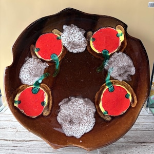 Peut inclure: Un plat de service en céramique marron avec un design unique. Le plat présente une série de formes circulaires rouges, jaunes et vertes, ainsi que des accents texturés blancs. Le bord a un bord irrégulier et ondulé.