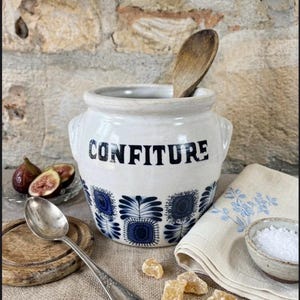 以下が含まれることがあります： 黒いハンドルと黒い太字の「But First, Coffee」の文字が入った白いセラミックマグ。マグは木製の表面に置かれています。マグの高さは10cmです。