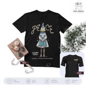 Könnte beinhalten: Schwarzes T-Shirt mit einer Illustration eines Charakters in einem blauen Kleid und Hut, sowie dem Wort "PEACE" in einer dekorativen Schriftart. Das T-Shirt hat auch japanischen Text und den Satz "SO BEAUTIFUL... IT NEVER GETS OLD MAGIC IS AMAZING!"