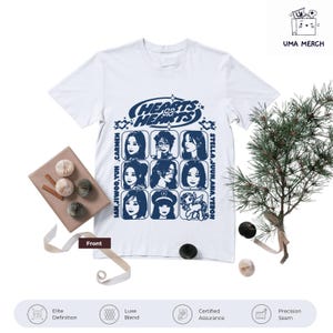 Puede incluir: Camiseta blanca con un diseño gráfico azul que presenta el texto "HEARTS HEARTS" y retratos de nueve personas. La camiseta también incluye el texto "JAN, JIWOO, YUN CARMEN" y "STELLA, JUUN, ANA, YEBON".