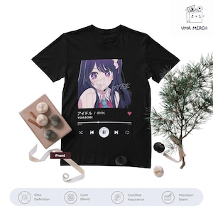May include: Black t-shirt featuring a graphic of an anime character with purple hair and the text "アイドル / IDOL YOASOBI". The design includes a music player interface. The shirt also has the text "UMA MERCH".