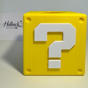May include: A bright yellow cube-shaped container featuring a raised white question mark on the front face. The cube has circular indentations at each of its four corners and a circular opening on the top surface. The text Holback Art Studio 3D is visible.