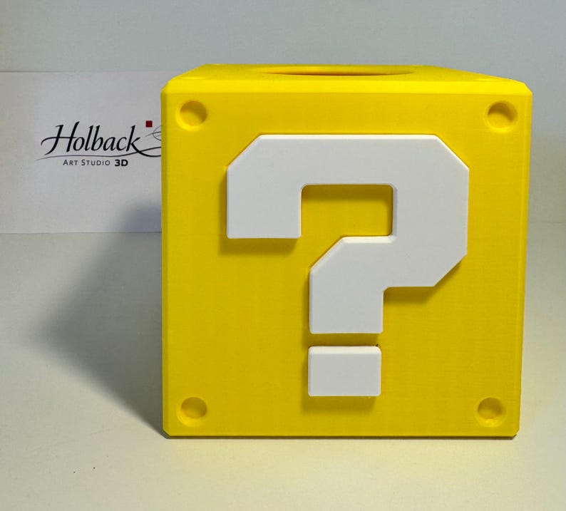 May include: A bright yellow cube-shaped container featuring a raised white question mark on the front face. The cube has circular indentations at each of its four corners and a circular opening on the top surface. The text Holback Art Studio 3D is visible.