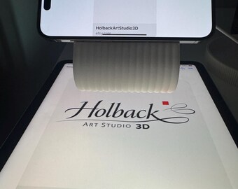 May include: A white, ribbed, cylindrical phone stand holding a smartphone horizontally. Both the smartphone and the tablet underneath display the logo for Holback Art Studio 3D, featuring the text Holback Art Studio 3D and the website etsy.com.