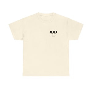 Könnte beinhalten: Cremefarbenes T-Shirt mit gesprenkelter Textur. Das Shirt zeigt den Text "ABI 2020" in schwarzen Blockbuchstaben auf der oberen linken Brust. Das Shirt hat einen Rundhalsausschnitt und kurze Ärmel.