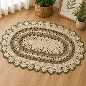 Puede incluir: Una alfombra ovalada hecha a mano con ganchillo, en tonos neutros. La alfombra presenta un centro color crema, rodeado de bandas verdes y marrones, con un borde festoneado. La alfombra mide aproximadamente 122 cm de largo y 76 cm de ancho.