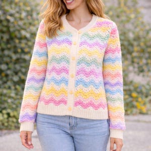 Puede incluir: Un cárdigan pastel con estampado de chevrón arcoíris con ribete y botones color crema. El suéter de manga larga presenta un cuello en V y está hecho de un material suave y texturizado. Los colores incluyen rosa, amarillo, azul y lavanda.