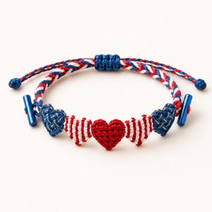 May include: A braided bracelet featuring a red, white, and blue cord with five heart-shaped charms. The center heart is solid red, flanked by two striped red and white hearts, and two blue hearts with gold accents. It includes blue metal toggle ends.