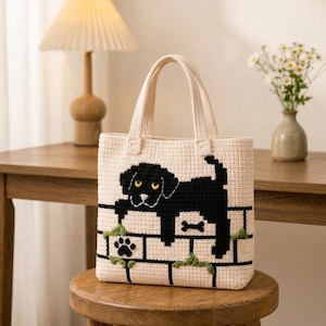 Può includere: Borsa tote all'uncinetto color crema con un disegno di cane nero su un motivo a muro di mattoni. Il cane è sdraiato con un osso e un dettaglio di impronta di zampa. La borsa ha due manici color crema.