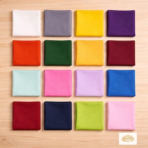 Può includere: Una collezione di sedici campioni di tessuto quadrati piegati in vari colori, tra cui bianco, grigio, giallo, viola, arancione, verde, bordeaux, azzurro, rosa, lavanda, blu e verde. I campioni sono disposti a griglia su una superficie di legno chiaro.