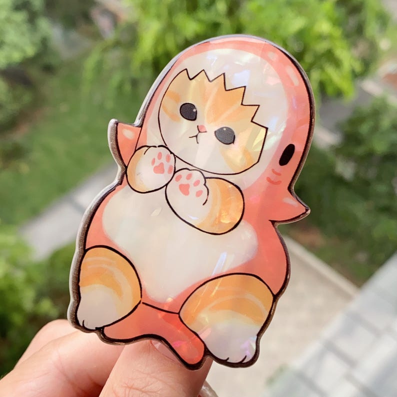 May include: A whimsical sticker featuring a cartoon cat dressed as a ghost. The design showcases a white and orange cat with pink paws and a ghost costume in shades of pink and orange. The sticker has a glossy finish.