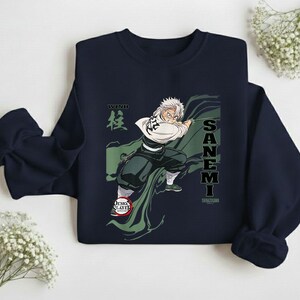 Puede incluir: Sudadera azul marino con un gr&aacute;fico de un personaje de la serie de anime Demon Slayer. El personaje se representa en una pose din&aacute;mica con una capa verde, y el nombre "SANEMI" est&aacute; impreso verticalmente. La palabra "WIND" tambi&eacute;n es visible.