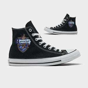 May include: Black high-top sneakers with white laces and soles. The Ravenclaw crest is displayed on the side of the shoe. The sneakers have a classic design with a canvas upper and rubber sole.