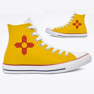 May include: High-top canvas sneakers in yellow with a white toe cap and sole. The sneakers feature the New Mexico Zia symbol in red on the side. The shoes have white laces and a red and blue stripe on the sole.