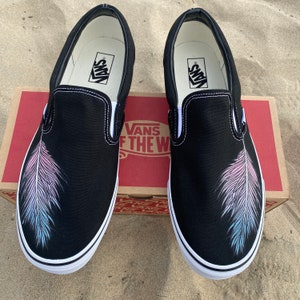 Puede incluir: Un par de zapatos Vans de lona negros con un dise&ntilde;o de pluma rosa y azul pintado en cada zapato.