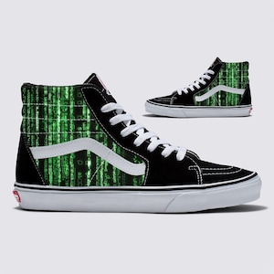 May include: High-top trainers in black and white, featuring a green digital rain design on the sides. The trainers have white laces, a white side stripe, and a white sole. A smaller version of the shoe is also shown.