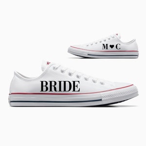 May include: A pair of white canvas sneakers with black text. One shoe says "BRIDE" and the other says "M♥C".