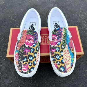 May include: Pair of white slip-on sneakers with colorful patchwork design. The design includes floral, leopard print, and text elements in various colors. The shoes are displayed on a brown cardboard box.