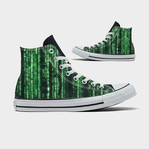 Könnte beinhalten: Hohe Canvas-Sneaker mit einem grünen und schwarzen Digital-Rain-Muster. Die Schuhe haben weiße Schnürsenkel, eine weiße Gummisohle und eine schwarze Zunge. Das Design erinnert an den Film Matrix.