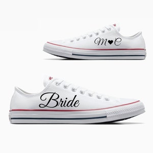 May include: A pair of white canvas sneakers with black text. One shoe says "Bride" and the other says "M♥E".