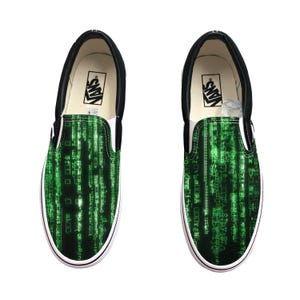 Può includere: Paio di scarpe slip-on nere e bianche con un motivo a pioggia digitale verde sul davanti. Le scarpe hanno una suola bianca e il logo Vans sulla soletta.
