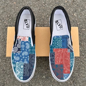 May include: A pair of black slip-on canvas shoes with a patchwork design featuring blue and red paisley patterns. The shoes have the word "BLVD" printed on the back.